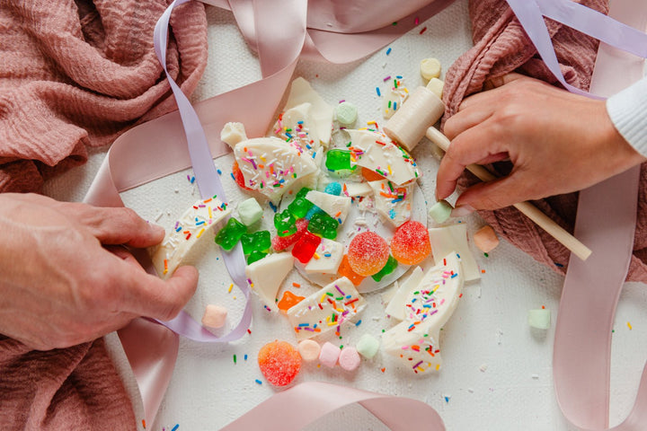 Decorative white chocolate bars with colorful candies and sprinkles on a pink surface.