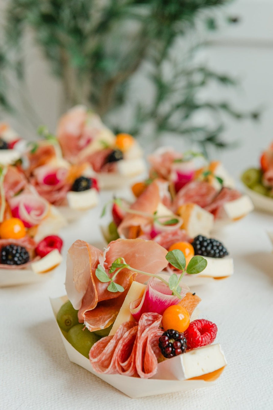 Plated appetizers with prosciutto, fruits, and vegetables on a white surface.