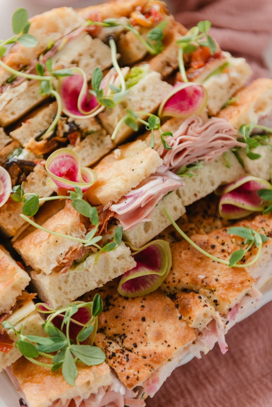 Stack of sandwiches with various fillings and garnishes on a plate.