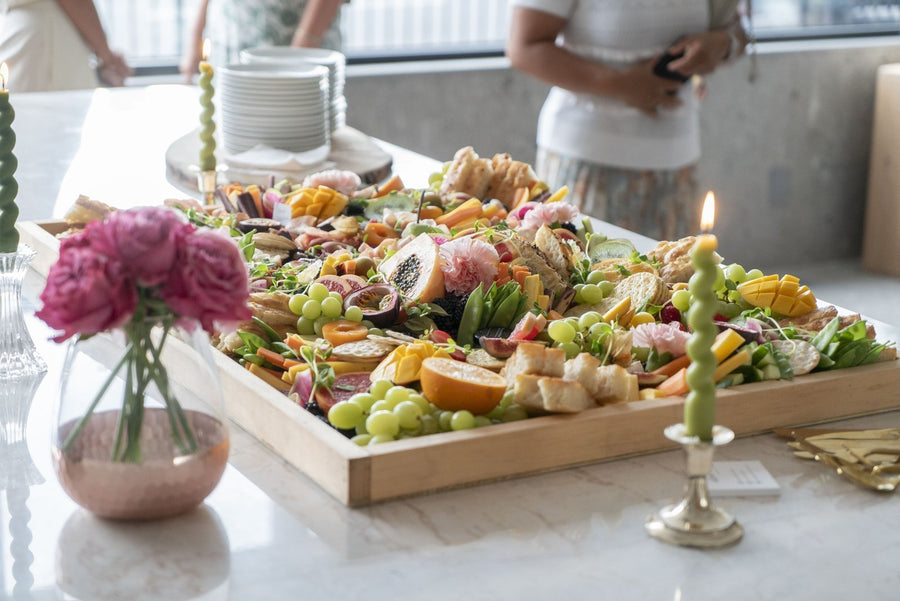 Platter of assorted fruits and cheeses on a table with candles and flowers.
