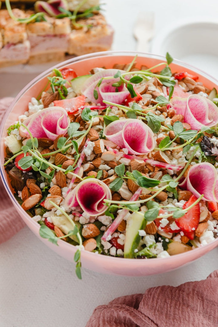 Salad with pink flowers and nuts in a pink bowl on a white surface