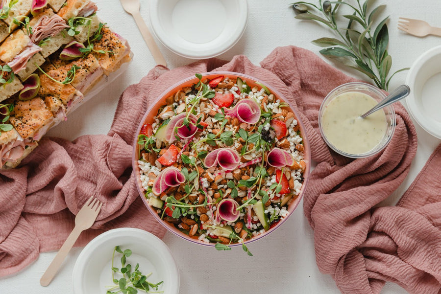 Salad with vegetables and pink flowers in a bowl on a white tablecloth with a pink cloth and side dishes.