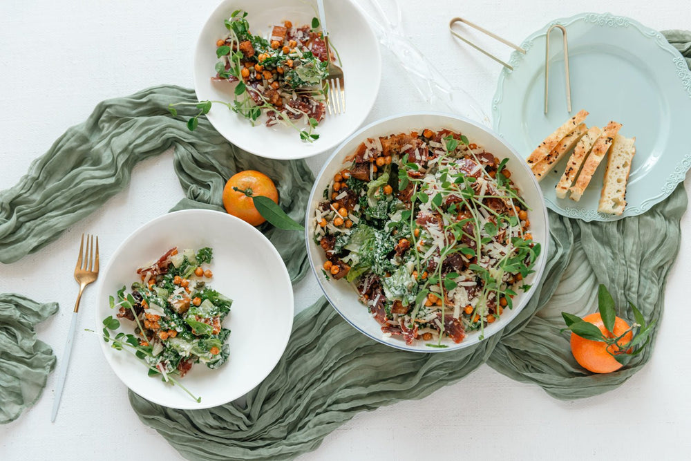 Three bowls of salad with a green cloth and oranges on a white surface