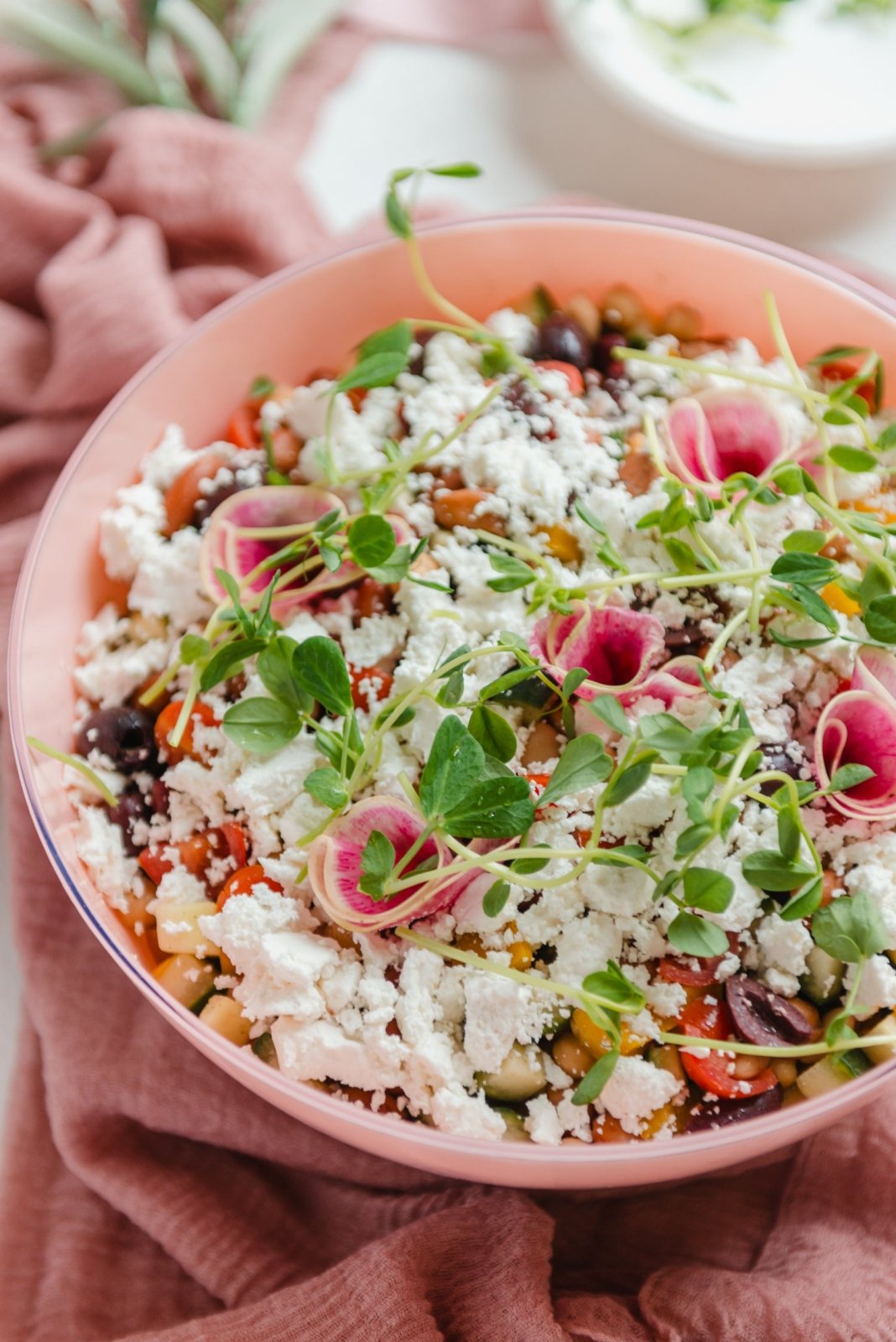Colorful salad with greens, pink pasta, and crumbled cheese in a pink bowl.