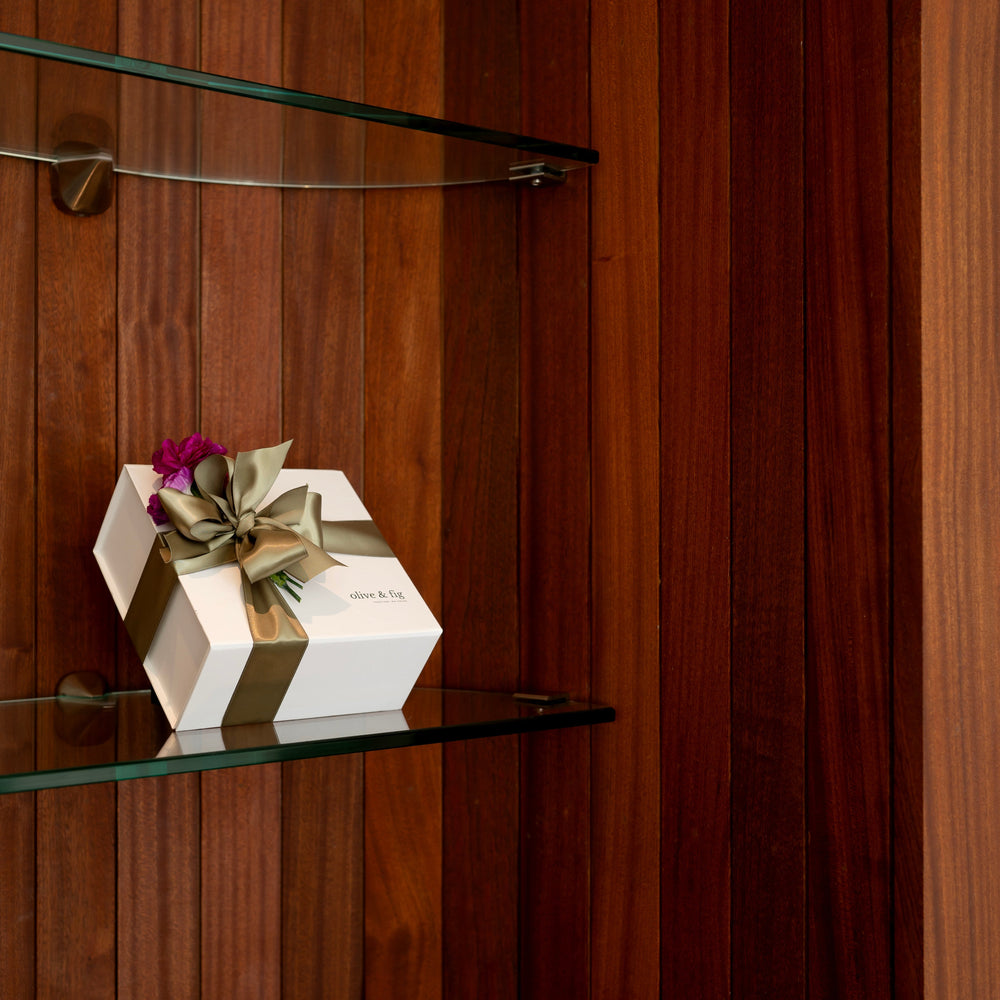 Decorative charcuterie box with a bow on a boutique glass shelf against a wooden wall