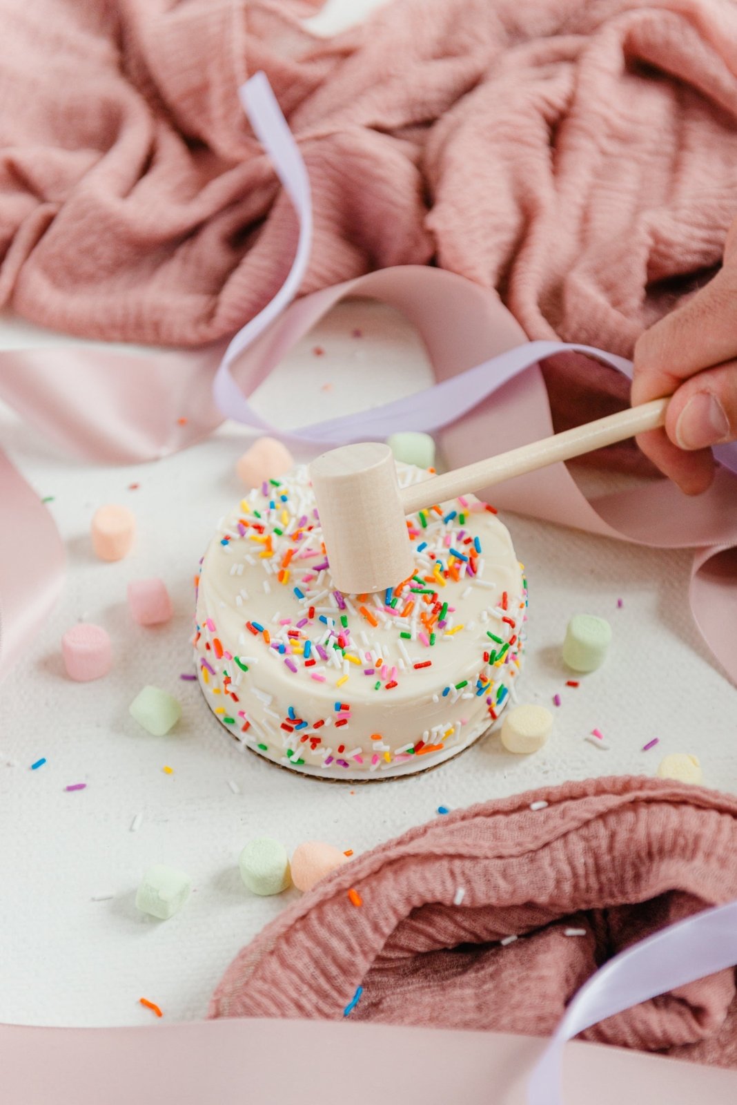 Donut with colorful sprinkles on a stick being held over a pink blanket