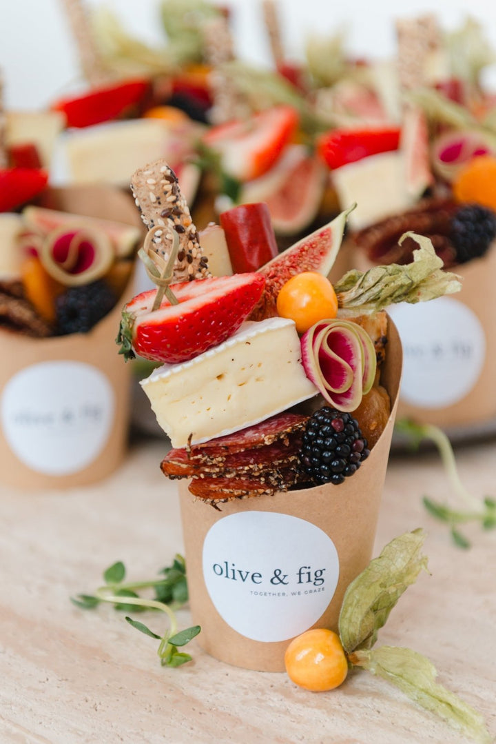 Dessert in a paper cup with fruits and cheese, branded 'olive & fig'.