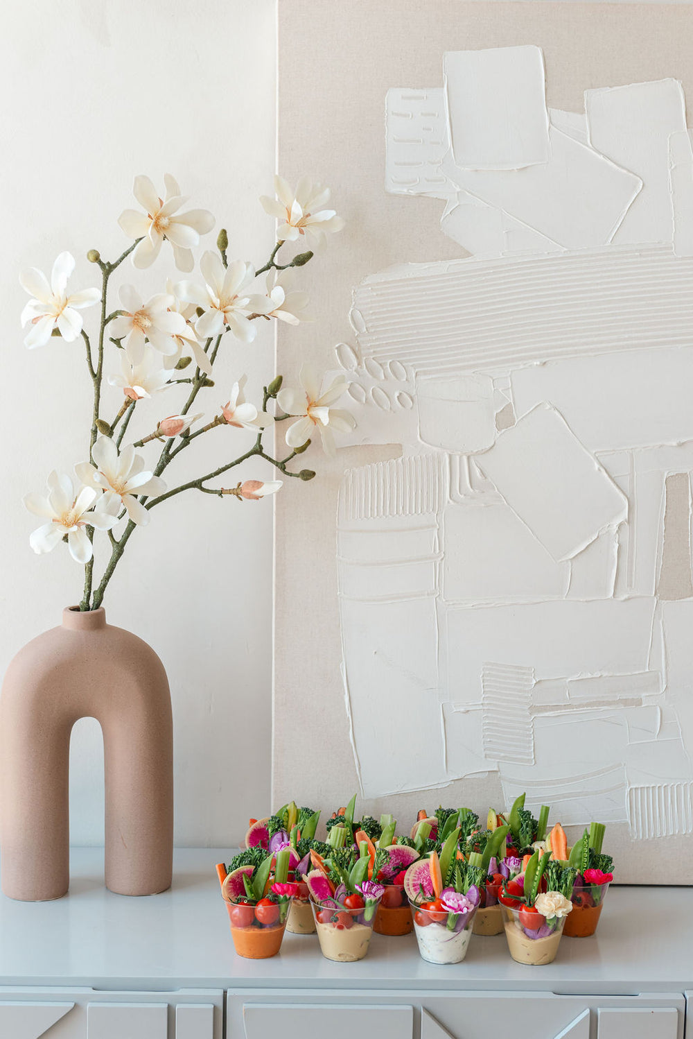 Vase with white flowers on a shelf with small potted plants below