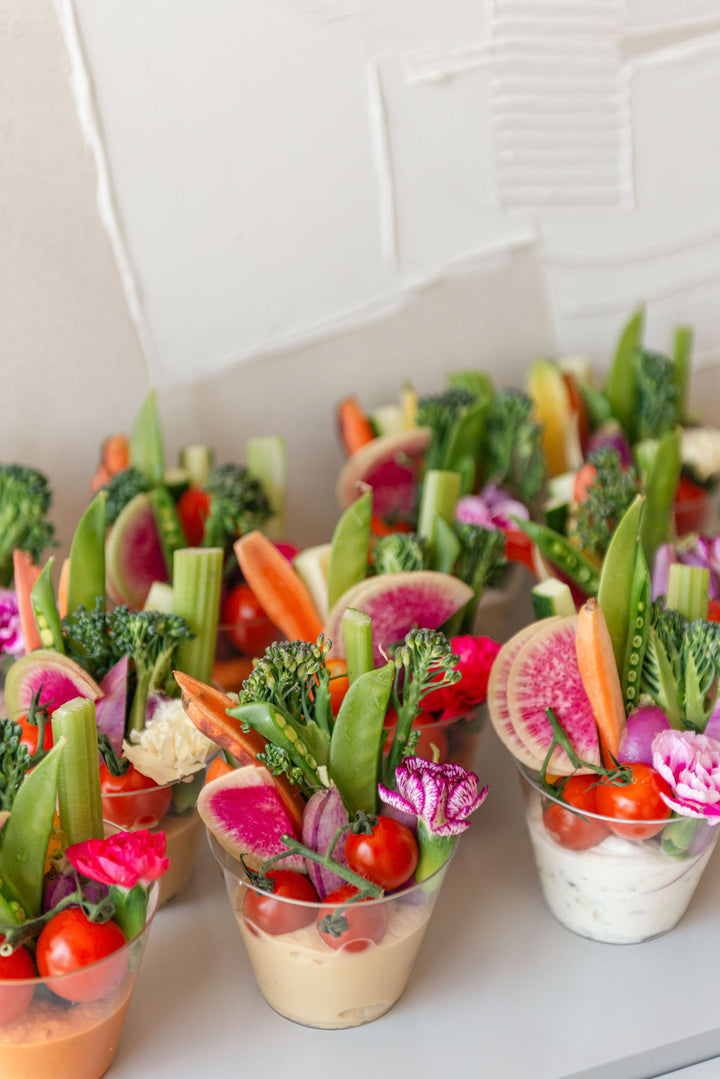 Assorted vegetables and fruits in small cups on a white surface