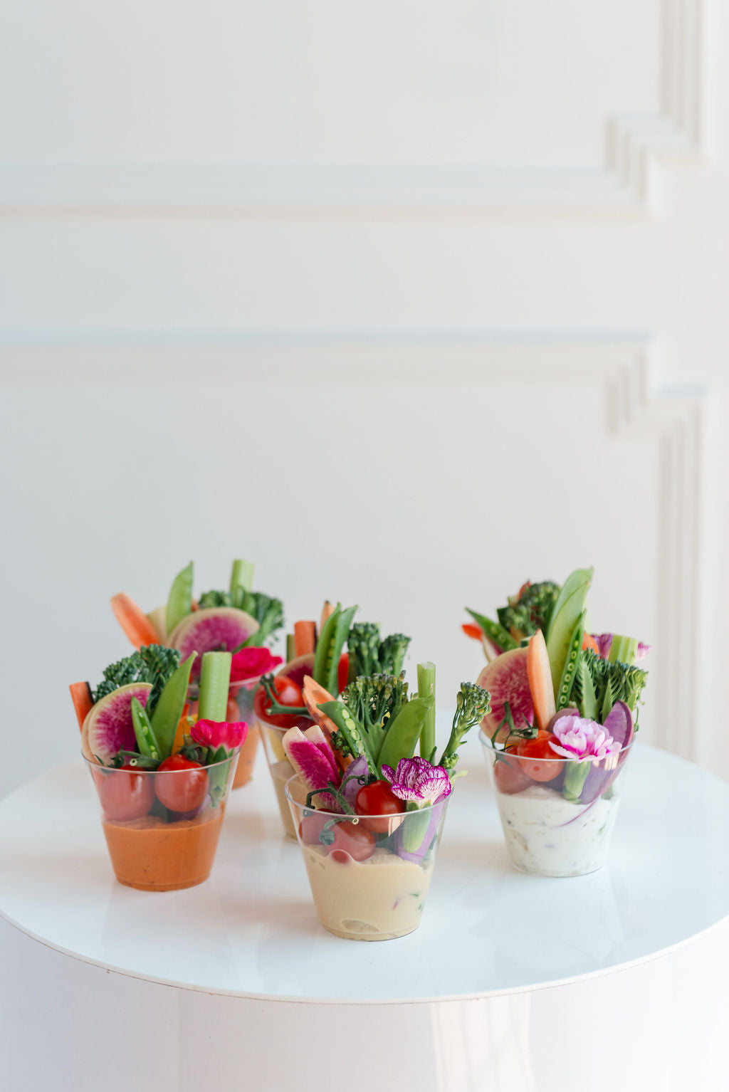 Four small cups filled with a colorful salad on a white surface.
