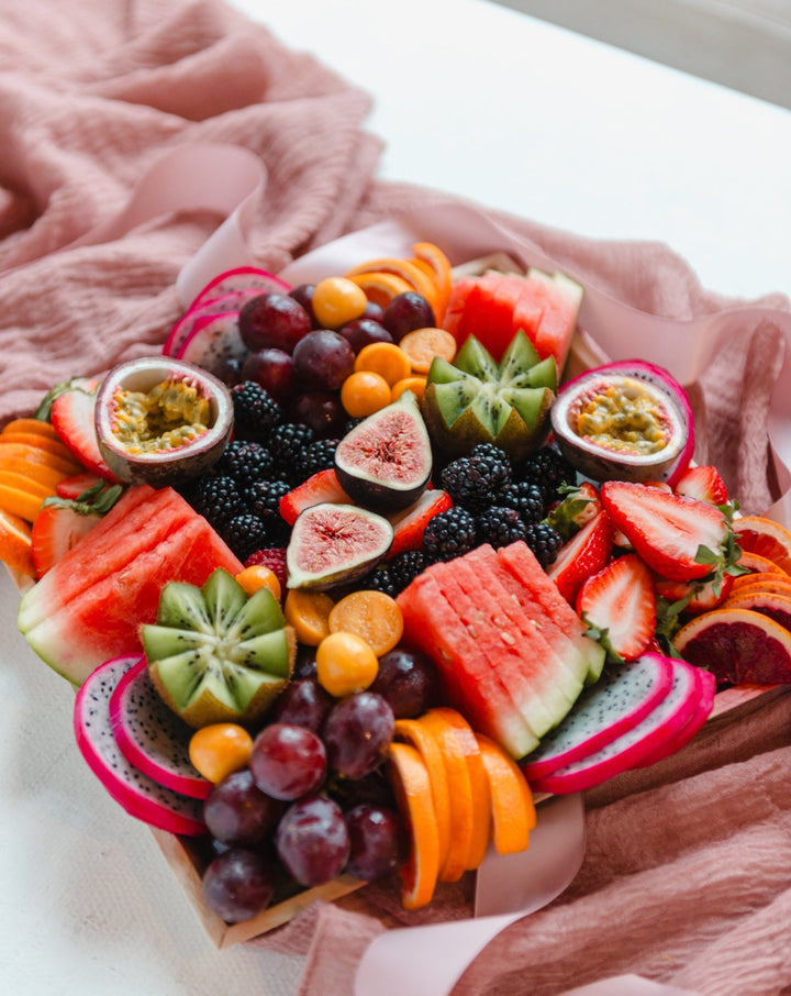 Assorted fruits including watermelon, kiwi, figs, and berries on a wooden board.
