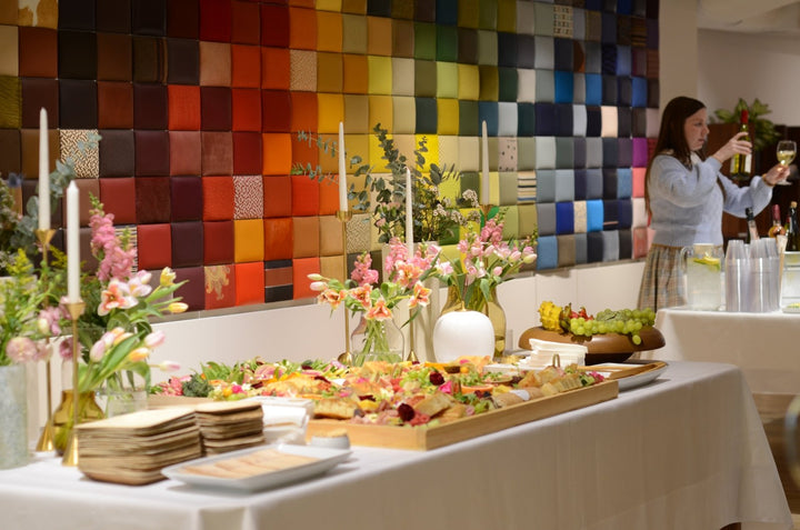 Buffet table with food and flowers against a colorful wall.
