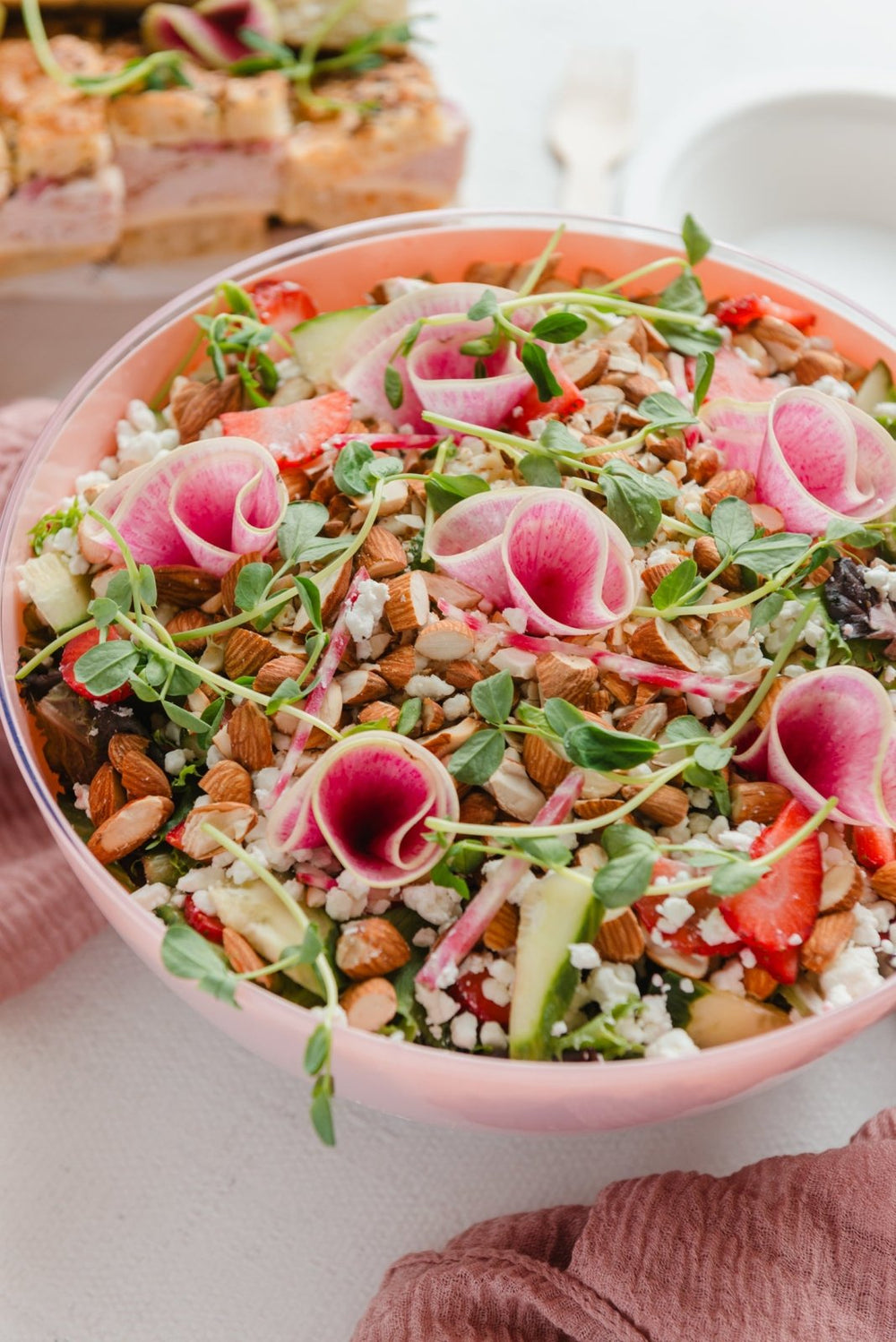 Salad with pink flowers and nuts in a pink bowl on a white surface