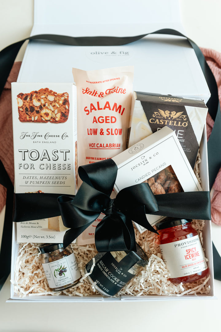 Gift basket with various items including a bottle of olive oil, a jar of jam, and a box of crackers.