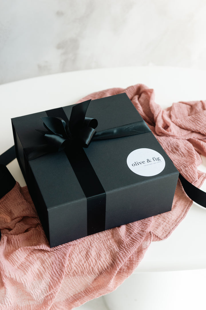 Black gift box with a bow and 'olive & fig' label on a pink fabric background