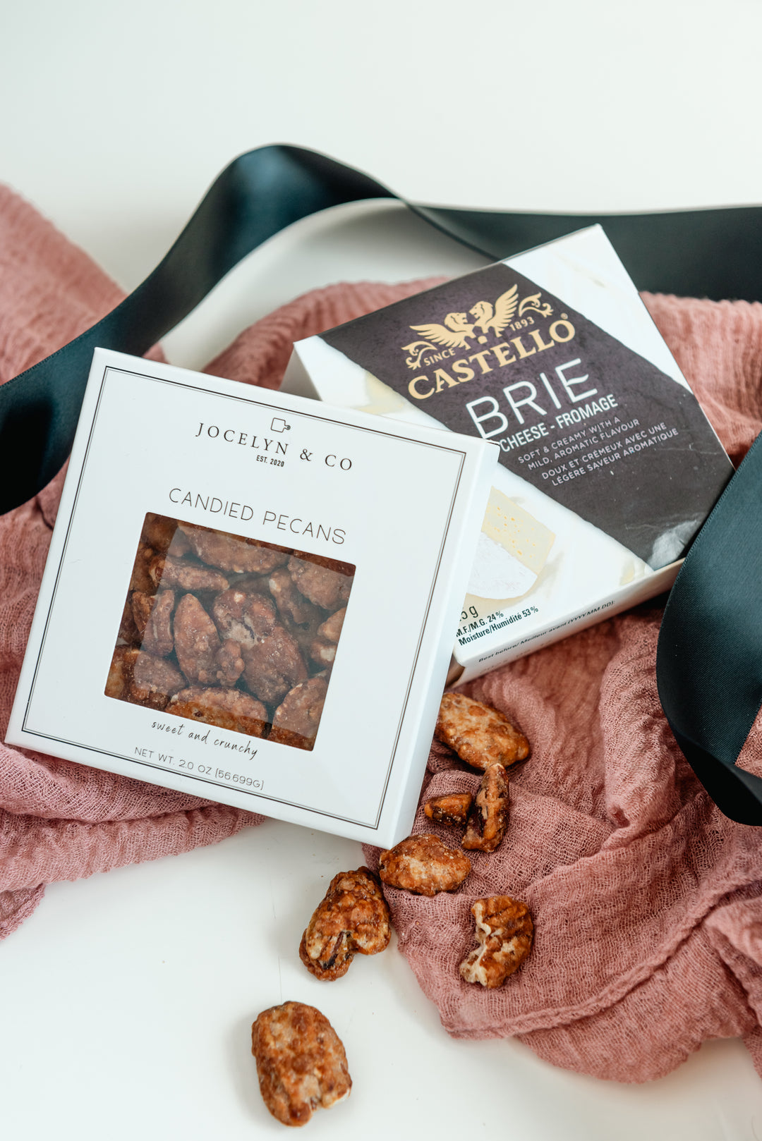 Box of Jocelyn & Co candied pecans and a block of Castello Brie on a pink cloth.