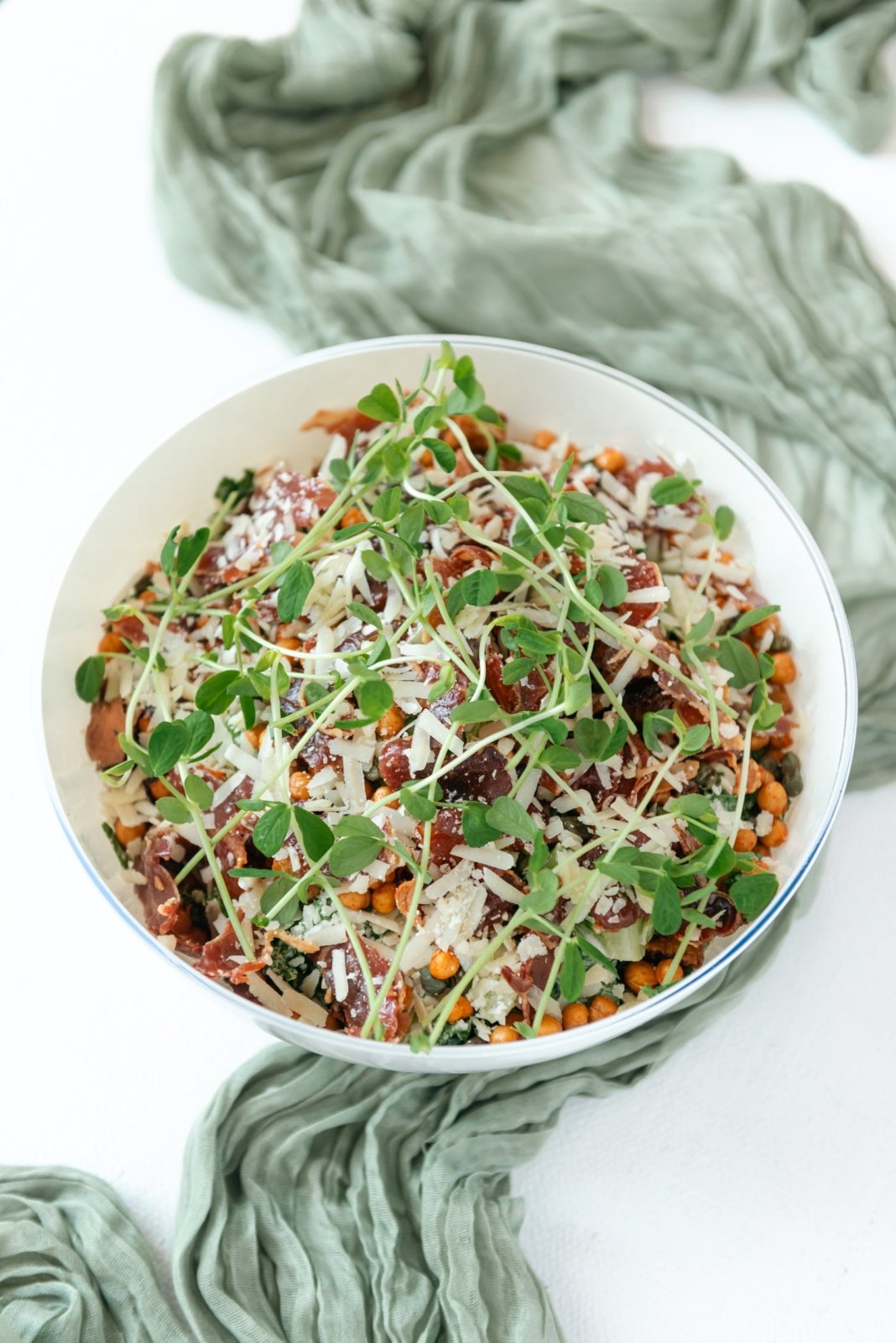 Salad with greens and other ingredients in a white bowl on a light background